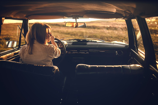 Young woman driving car on beautiful sunny day, getting away from it all alone, rear view, photo is taken in car from 1980 year