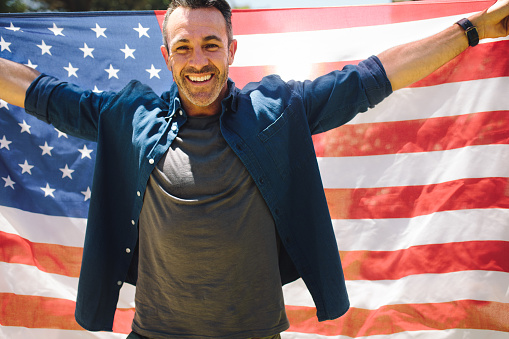Portrait of a smiling man holding a large american flag behind him. Man celebrating an occasion carrying the american flag behind him.