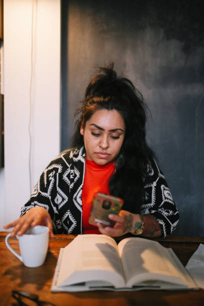 Vintage toned portrait of a young Latinx woman, sitting in her apartment in downtown Los Angeles, reading a book, going through the paperwork. She is finishing up her work late in the evening.