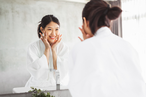 Mujer asiática limpieza cara frontal de espejo, cuidado de la piel y el concepto de eliminación cosmética photo