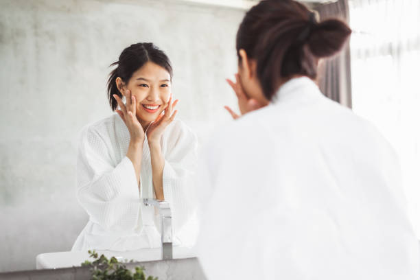 donna asiatica che pulisce il viso davanti allo specchio, cura della pelle e concetto di rimozione cosmetica - lavarsi il viso foto e immagini stock