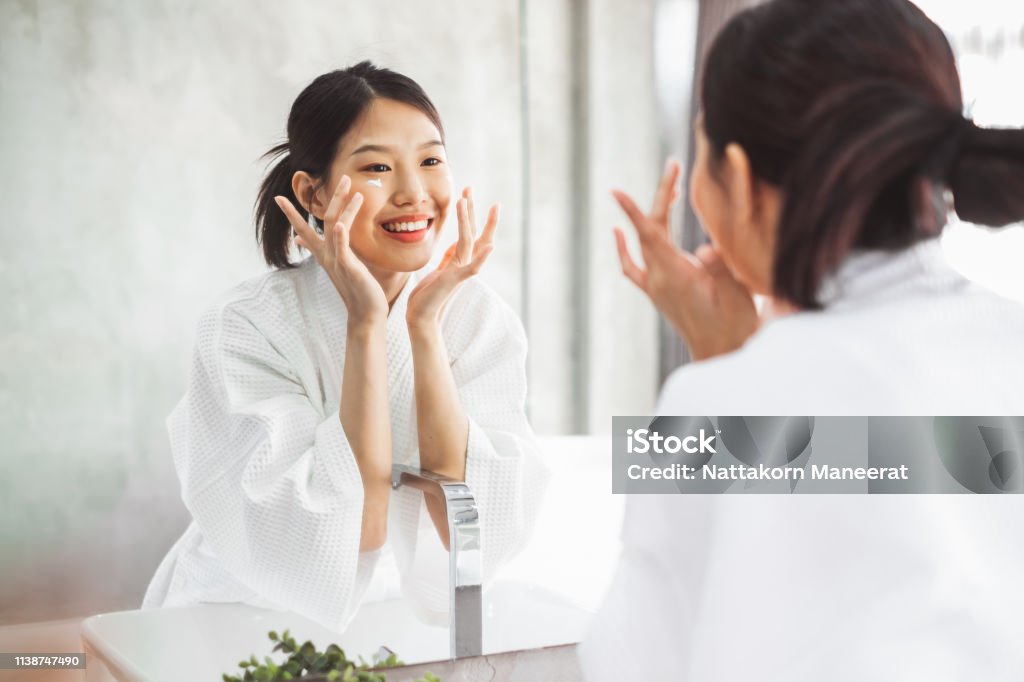 Asian woman cleaning face front of mirror, skin care and cosmetic removal concept Asian and Indian Ethnicities Stock Photo
