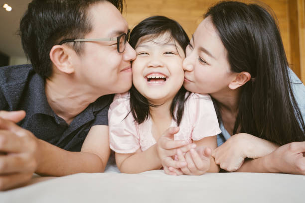 asiatische eltern küssen ihre kleine tochter auf beiden wangen. familienporträt. - ostasiatischer abstammung fotos stock-fotos und bilder