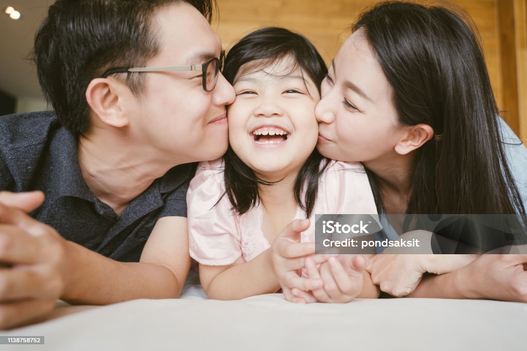 Asian Parents kissing their little daughter on both cheeks. family portrait. Family Stock Photo