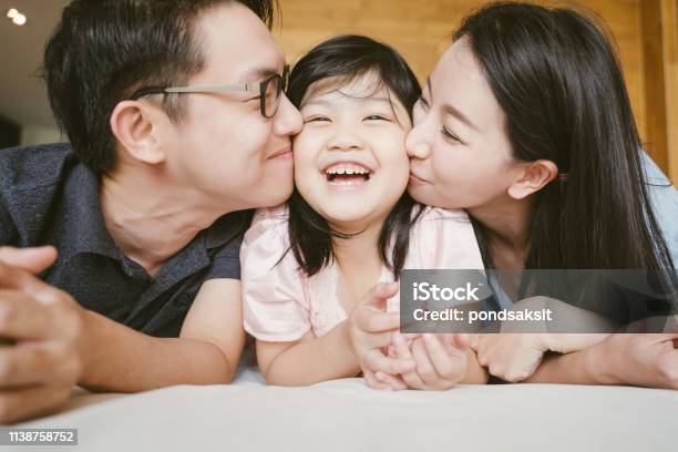 Asian Parents Kissing Their Little Daughter On Both Cheeks Family Portrait Stock Photo - Download Image Now