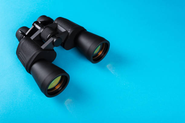 istock Black binoculars with orange lens on blue background 1138759840