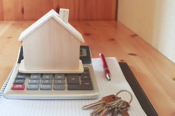 Paper notebook with calculator, house model keys and pen on wooden table.  House building, buying or renting new home planning concept.