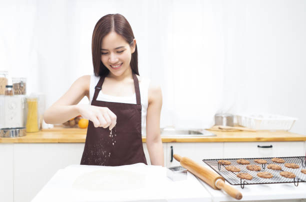 mulher asiática bonita que prepara a massa de pão para bolinhos, polvilhando a farinha branca sobre a massa de pão crua na cozinha - baker california - fotografias e filmes do acervo