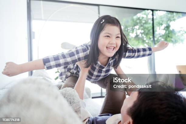 Happy Little Girl Daughter Playing With Father While Ride Dad Back And Dad Lying On The Bed At Home Stock Photo - Download Image Now