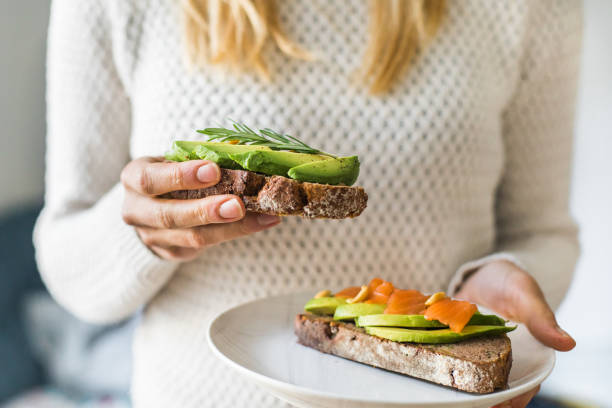 primo piano della donna che tiene piatto con toast all'avocado come spuntino fresco, luce del giorno. - fatty acid foto e immagini stock