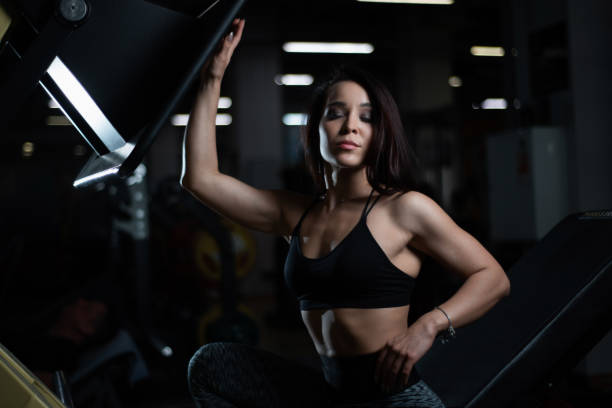 fille de remise en forme posant dans la salle de gym, exhibant son corps et relaxant après une séance d'entraînement - showing off muscular build the human body human muscle photos et images de collection