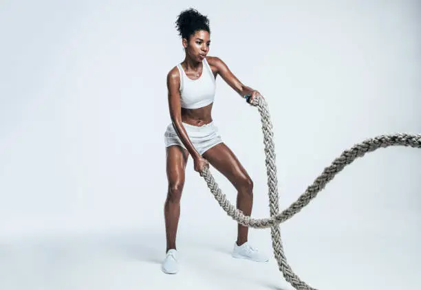 Fitness woman using training ropes for exercises. Athlete working out with battle ropes on white background.