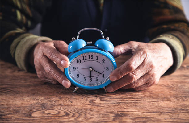 istock Elderly woman hands with alarm clock. Time 1138789593