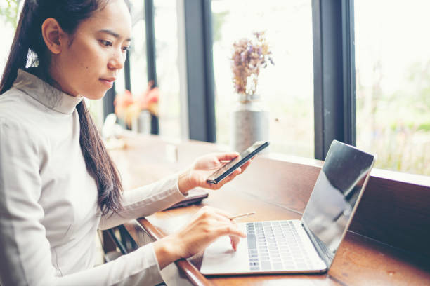 istock Side View Of Woman Using Mobile Phone And Laptop On Table 1138792302