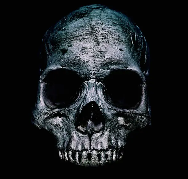 An old human skull showing scratch marks and erosion against a black background.