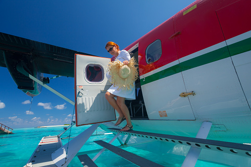luxury travel theme wealthy woman exiting on tropical island disembarking from seaplane on sunny vacation day with clear blue sky