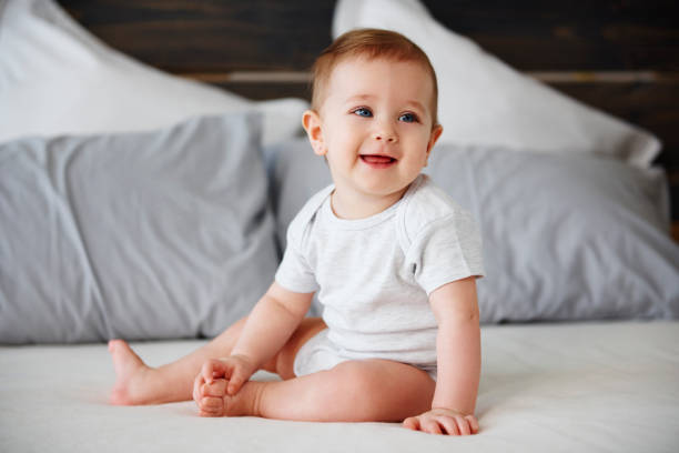ベッドの上に座る笑顔の赤ちゃん - 生後6ヶ月から11ヶ月 ストックフォトと画像