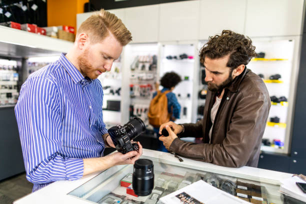 istock Camera store salesman demonstrating various camera lenses on a mirrorless camera to his customer in a camera shop 1138810583