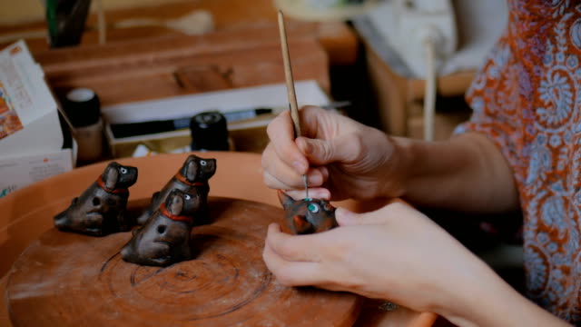 Professional potter painting ceramic souvenir penny whistle in pottery workshop