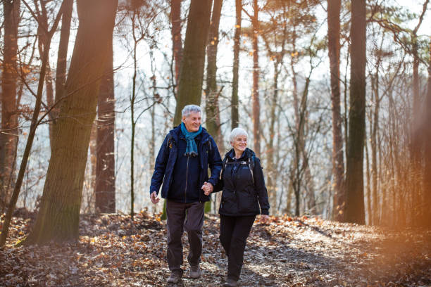 Beautiful senior couple on a hike Beautiful senior couple on country walk. Elderly man and woman holding hands and walking through a forest trail. grunewald berlin stock pictures, royalty-free photos & images