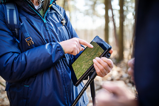 Senior man with friends reading a map on his digital tablet while on a country walk. Cropped shot of man using tablet computer to find the right direction during hiking trip.