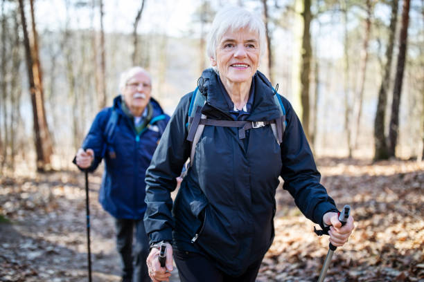 Senior woman hiking with friend Beautiful senior woman walking in front with a man behind on a forest trail. Senior people on a country walk. grunewald berlin stock pictures, royalty-free photos & images