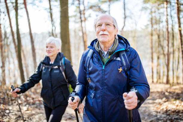 Senior man hiking with friend Retired senior man walking in front with a woman behind on a forest trail. Elderly people on a country walk. grunewald berlin stock pictures, royalty-free photos & images