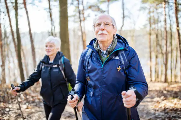 Retired senior man walking in front with a woman behind on a forest trail. Elderly people on a country walk.