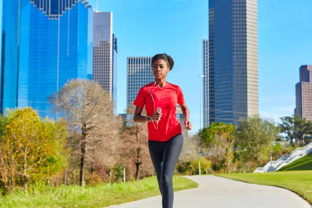 Runner girl running and listening music earphones in the city park