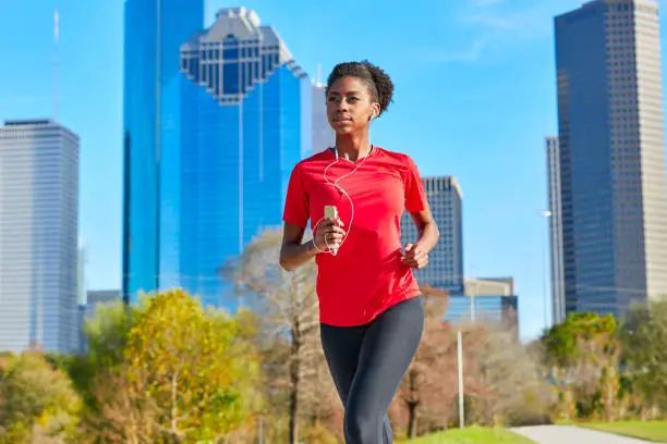 Runner girl running and listening music earphones in the city park