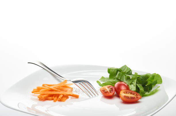 Homemade mixed salad with iceberg and slices of small peppers served in a salad bowl with a fork on a white background
