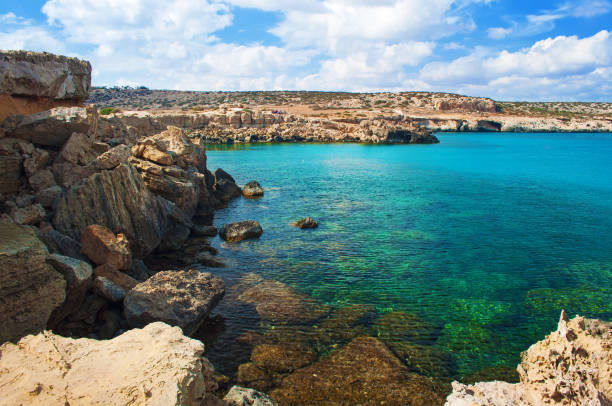 immagine della baia della laguna blu vicino a capo greco, cipro. vista della costa rocciosa vicino all'acqua di smeraldo trasparente verde profondo contro una collina rocciosa. incredibile paesaggio nuvoloso. giornata calda in autunno - beauty in nature cloud rocky coastline rock foto e immagini stock