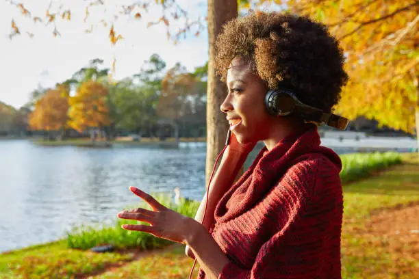 Woman listening music in the autumn park at sunset with headphones