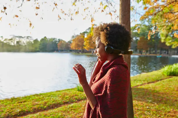 Woman listening music in the autumn park at sunset with headphones