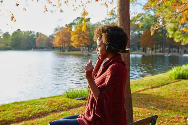 Woman listening music in the autumn park at sunset with headphones