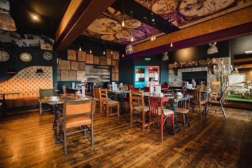 Wide shot angle of an empty restaurant showing the rustic style of interior design with mismatched chairs and quirky wall designs.