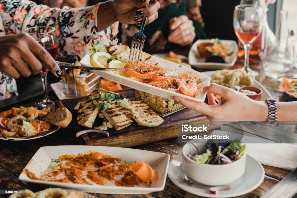 Sharing is Caring Point of view image of a group of multi-ethnic friends sharing multiple dishes, with a plate of prawns as the main focus. Restaurant Stock Photo