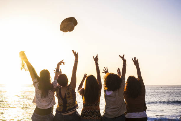 estate e felicità per il viaggio e il concetto di freindship con un gruppo di ragazze felici viste dal retro che si godono e celebrano il tramonto e il mare insieme lanciando cappello e rinunciando - fourty five foto e immagini stock