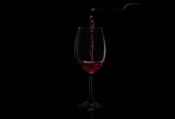 Red wine on black background Red wine pouring in a glass from a bottle. Studio shot on black background. merlot grape photos stock pictures, royalty-free photos & images
