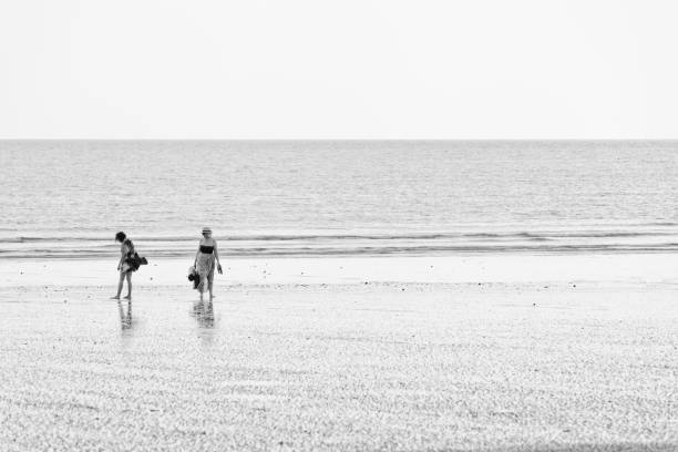 Pakarang beach (Takua Pa) at sunset.  Two women walking on Pakarang beach near the water's edge in Thailand.