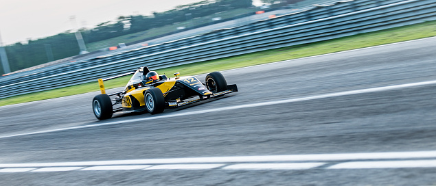 Panning shot of a zooming black and yellow formula race car on the track.
