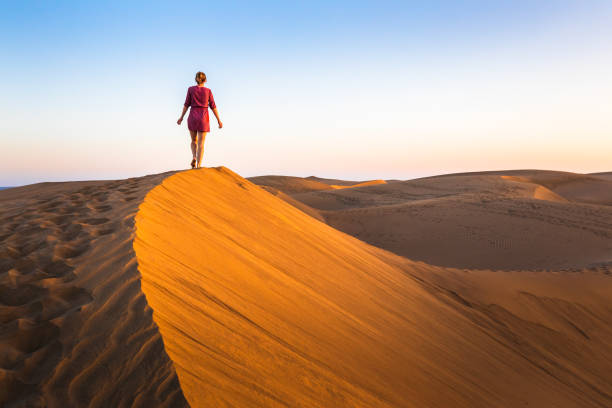 ragazza che cammina sulle dune di sabbia nel deserto arido al tramonto e indossa abiti, paesaggio panoramico del sahara o del medio oriente - vacations tourism travel white sand foto e immagini stock