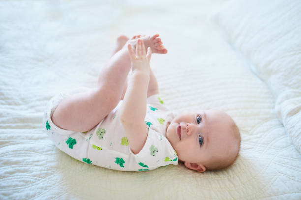 Cute baby girl lying on her back Cute baby girl lying on her back and touching her feet. Happy healthy kid at home in nursery 8 weeks stock pictures, royalty-free photos & images
