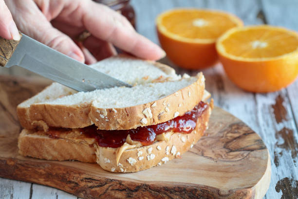 kobiety hand cutting masło orzechowe i strawberry jelly sandwich - frey zdjęcia i obrazy z banku zdjęć