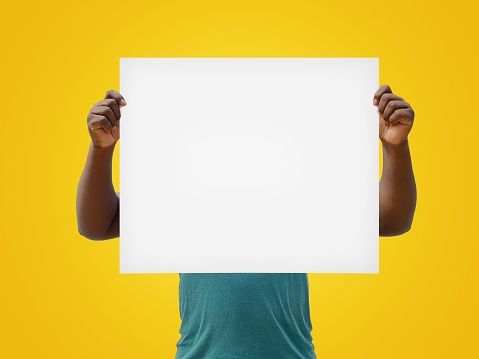 African man holding a blank white sign over his face, isolated on a yellow background