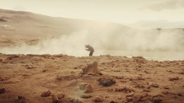 Young african ethnicity man dancing on a geothermal area. Geysers in background