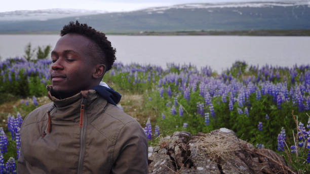 African man meditating surrounded by flowers. Open arms
