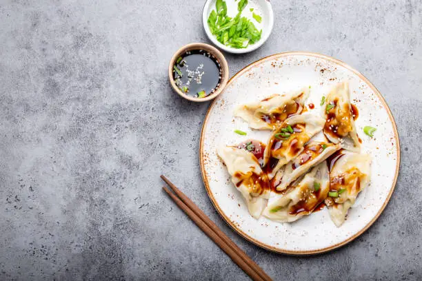 Close-up, top view of traditional Asian/Chinese dumplings on white plate with soy sauce and chopsticks on gray rustic stone background with space for text. Authentic Chinese cuisine, copy space