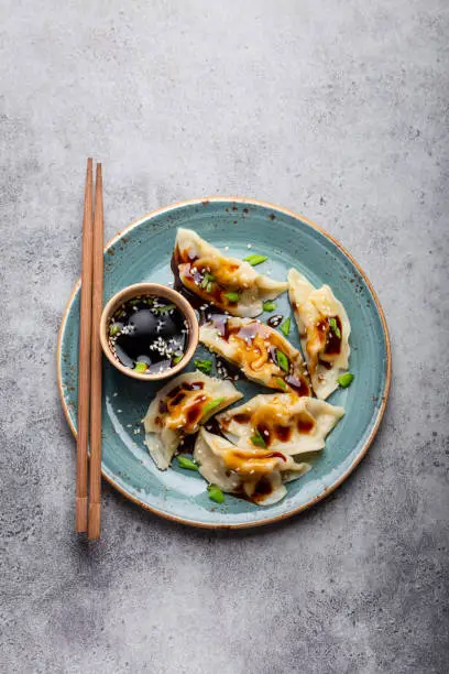 Close-up, top view of traditional Asian/Chinese dumplings in blue plate with soy sauce and chopsticks on gray rustic stone background. Authentic Chinese cuisine