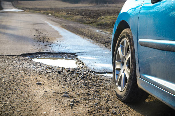 автомобиль и зимняя выбоина на открытой дороге - pot hole стоковые фото и изображения